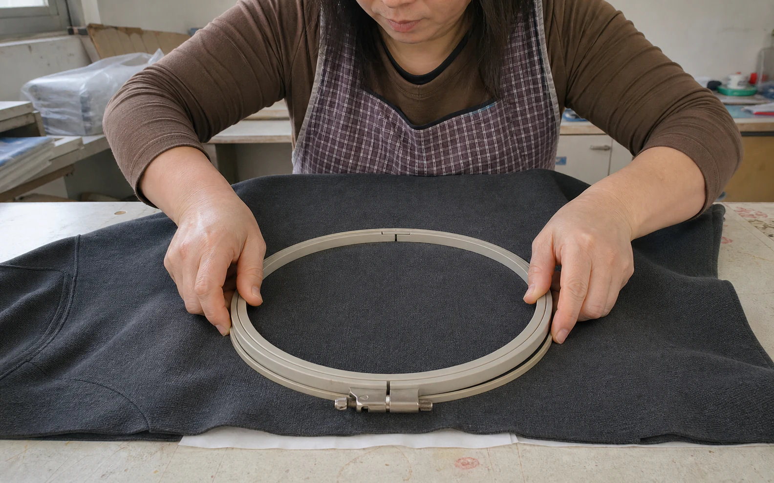 Worker hooping a knit garment with backing on a flat table