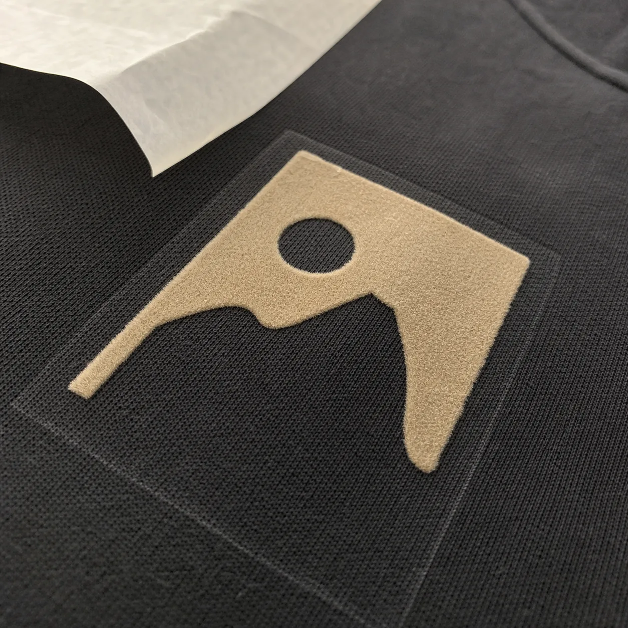 Flock transfer edge lifting beside a thick garment seam