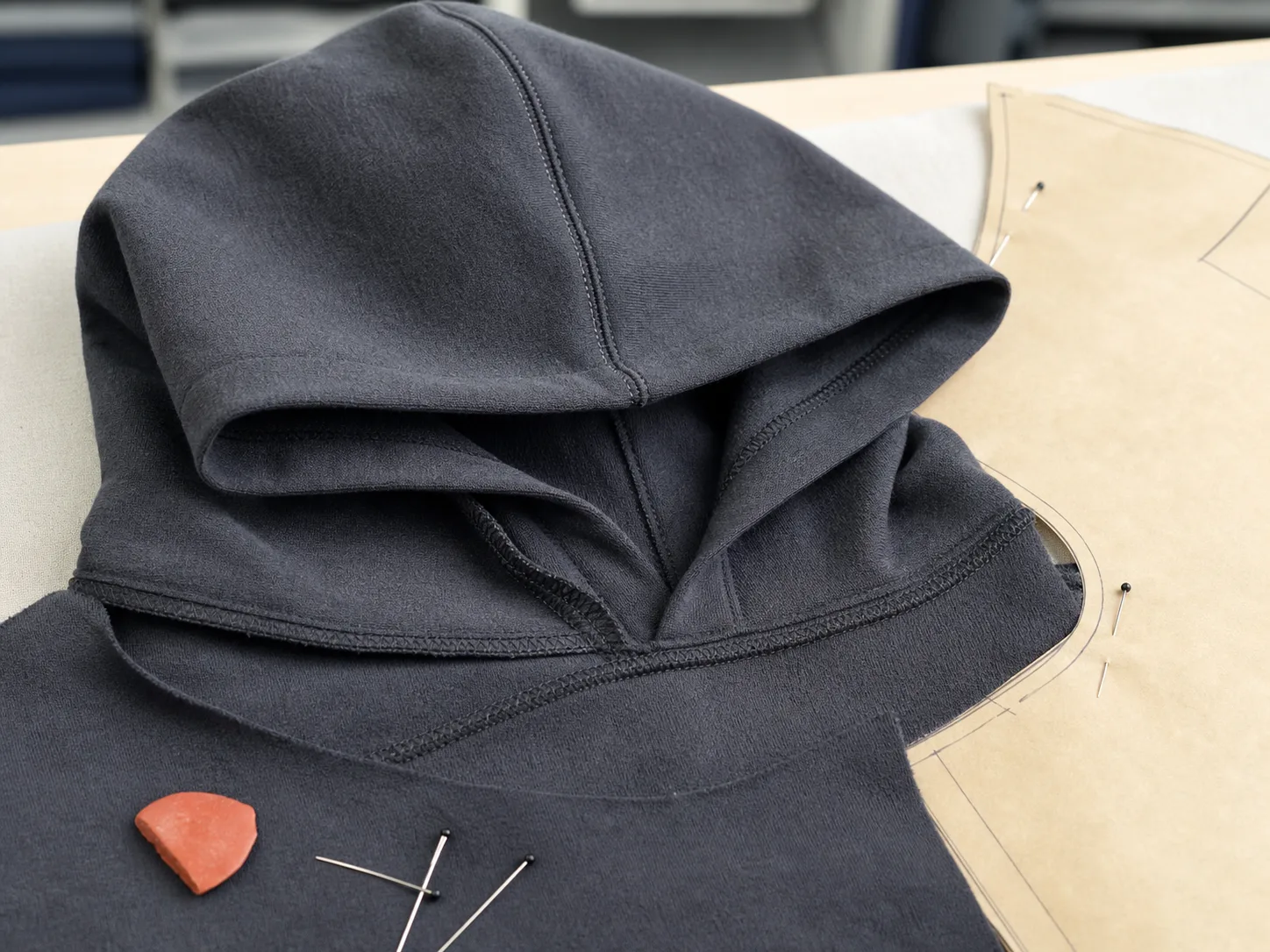 Two-piece hoodie hood and neckline seam shown beside a pattern piece during sample construction.