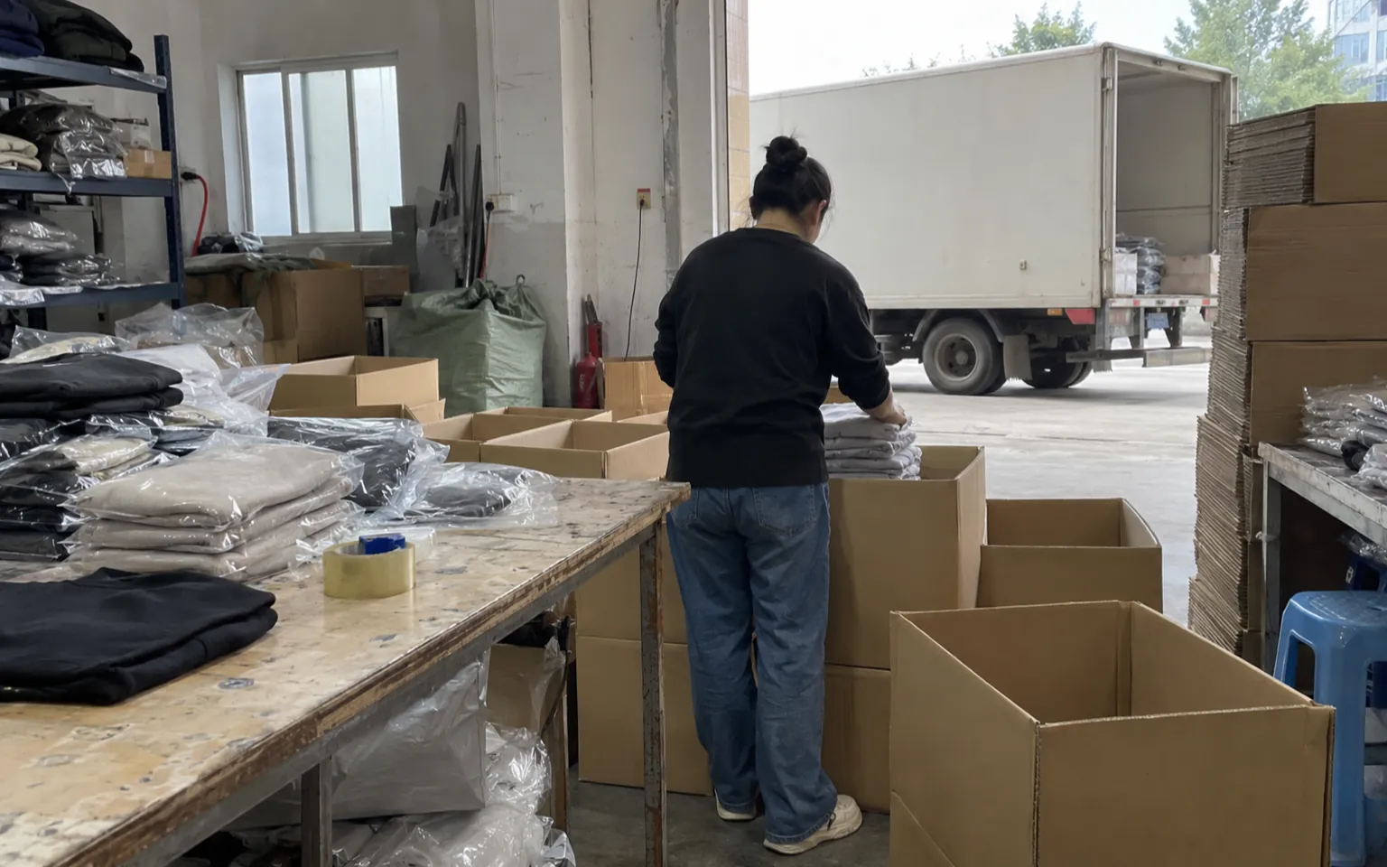 Des vêtements pliés sont emballés dans des cartons près d’une porte de chargement.