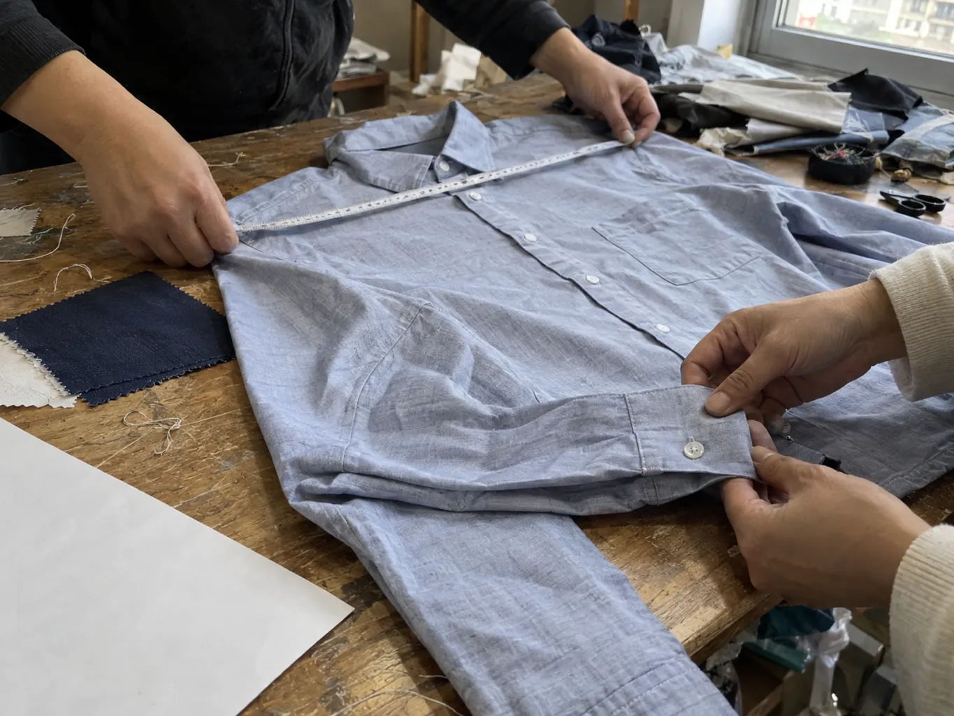 Hands measure a shirt sample and inspect its cuff seam.