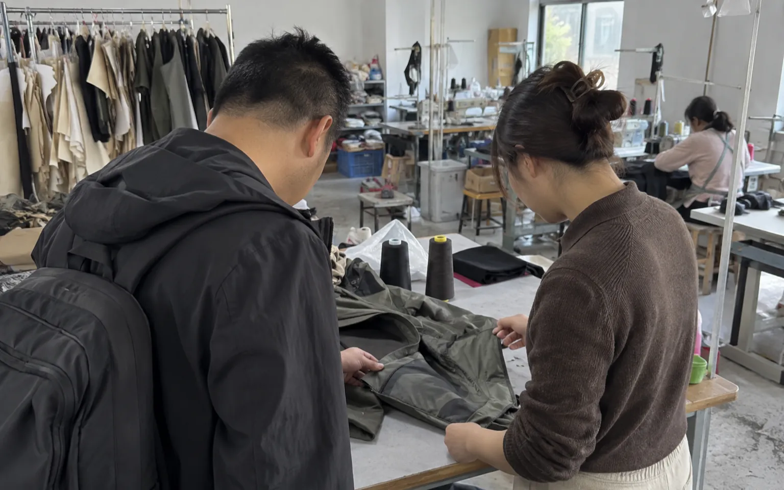 Two people inspect a jacket sample at a workshop table.